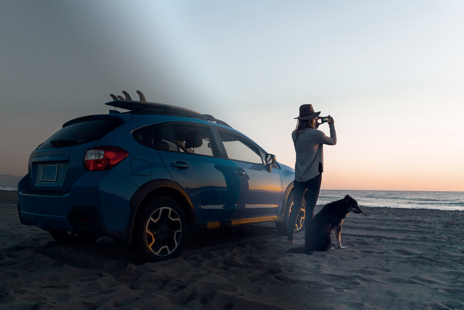 Woman photographing while standing with dog by car at the beach.