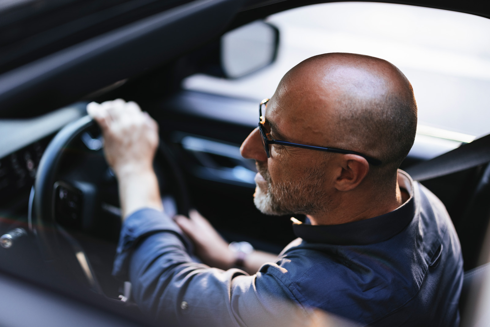 A businessman is seen driving a car through a sunny urban city. The image conveys a sense of independence and focus while navigating the bustling streets.